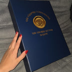 Blue book titled 'The Vampire Diaries' held by a hand on a gray surface
