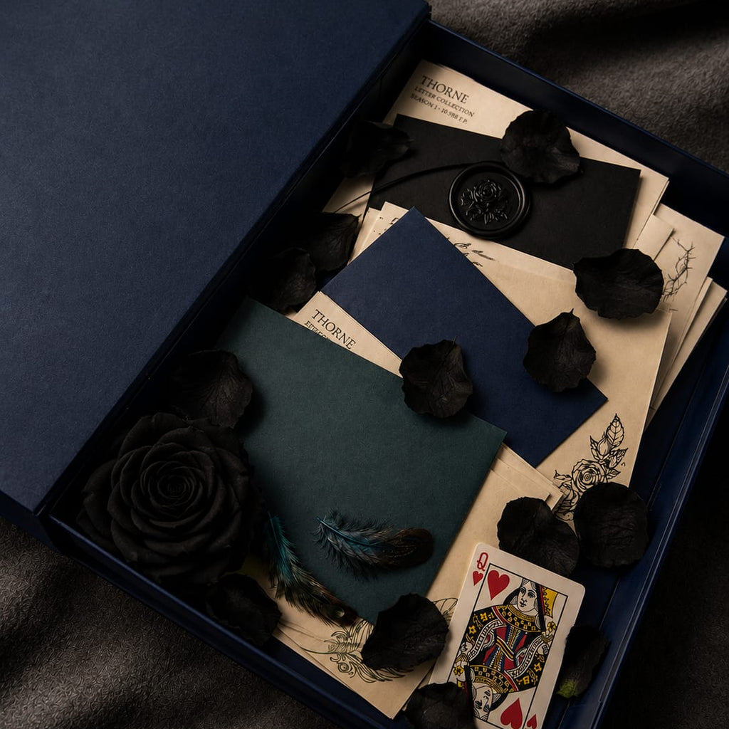 Decorative box with playing cards, envelopes, and black roses on a dark fabric background