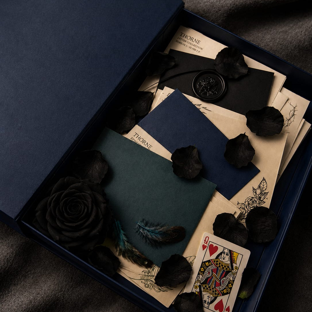 Decorative box with playing cards, envelopes, and black roses on a dark fabric background
