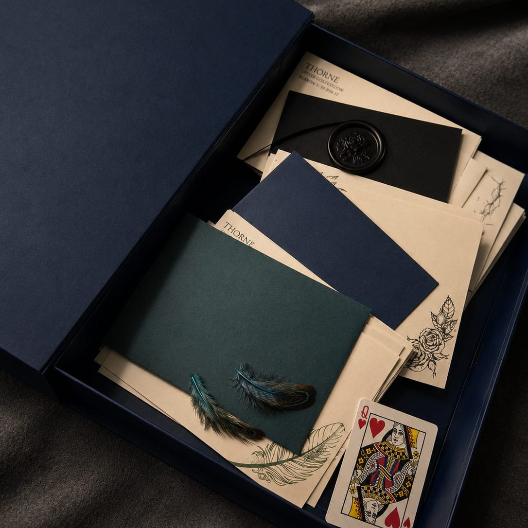 Collection of playing cards and stationery items in a dark blue box on a dark fabric background
